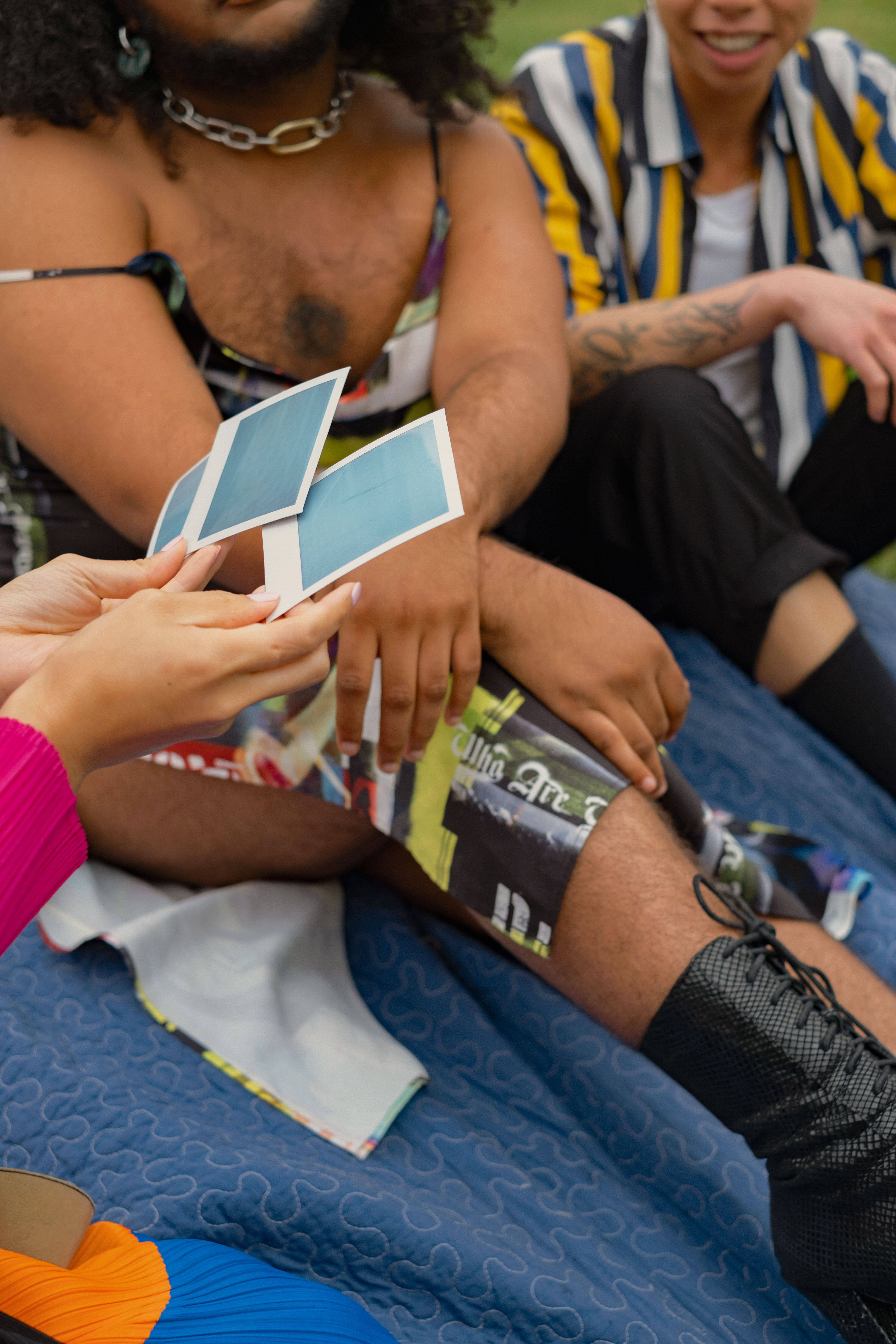 Three friends of varying genders looking at polaroids in a park